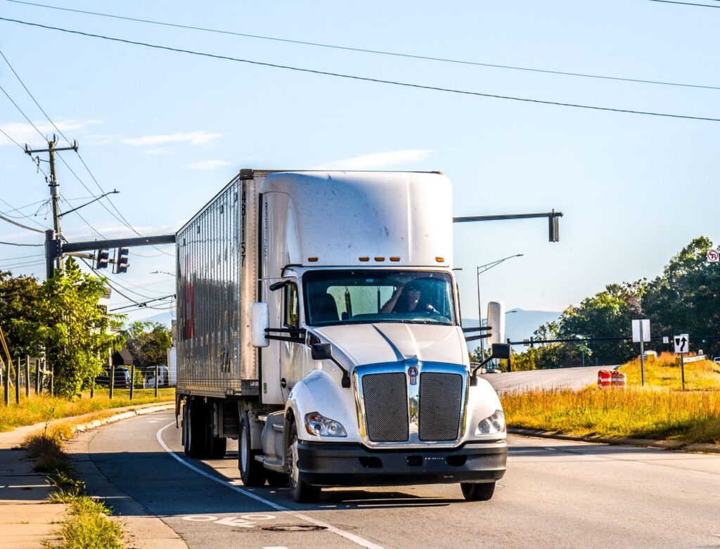 White semi truck pulling a dry van trailer down a highway on a sunny day, a common purchase for owner-operators checking what credit score they need to finance a semi truck