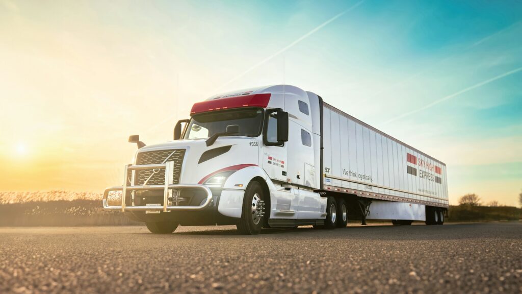 White semi truck with a 53-foot dry van trailer parked on an asphalt lot at sunset.