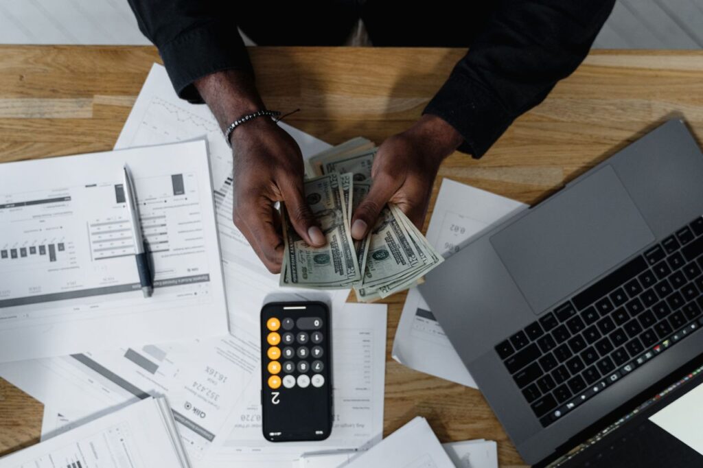 Person counting cash over financial reports, a phone calculator, and a laptop while budgeting for a truck purchase
